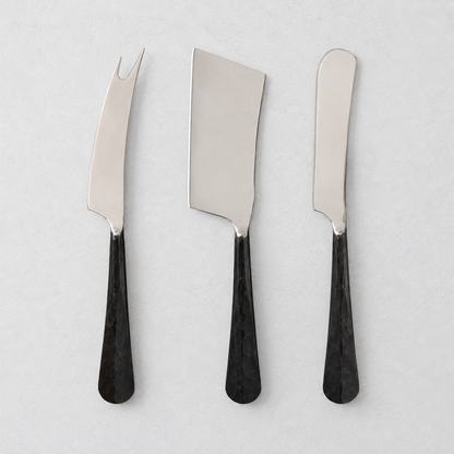 Three-piece cheese knife set with stainless steel blades and black, hand-forged, hammered metal handles.