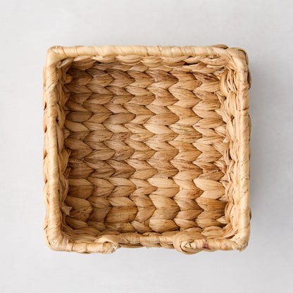 Square woven water hyacinth cocktail napkin holder with a natural tan finish and side cutouts.