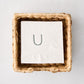 Square woven water hyacinth cocktail napkin holder with white monogrammed napkin inside.