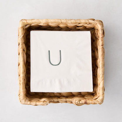 Square woven water hyacinth cocktail napkin holder with white monogrammed napkin inside.