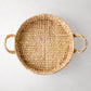 Round woven hyacinth tray with natural light brown fibers and two side handles, top-down view.