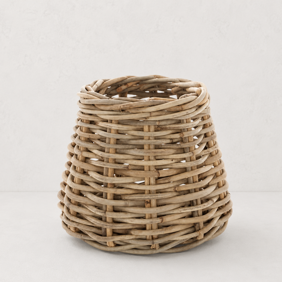 Small conic basket made of natural sandblasted rattan with a rustic woven texture on a neutral background.