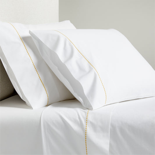 White percale sheet set with yellow diamond embroidered detail on pillowcases and flat sheet.