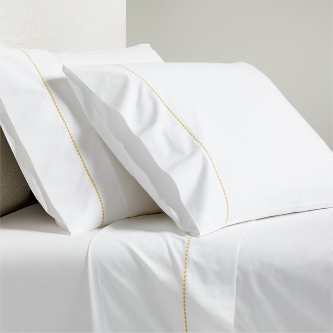 White percale sheet set with yellow diamond embroidered detail on pillowcases and flat sheet.
