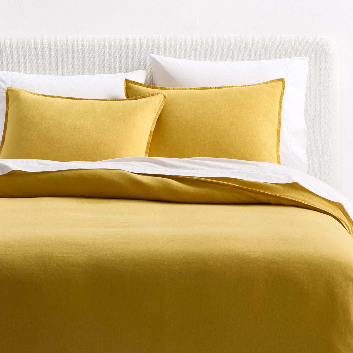 Yellow European washed linen duvet cover and shams set with a relaxed, textured finish on a white upholstered bed.