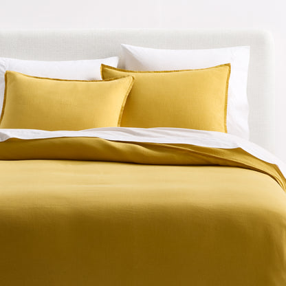 Yellow European washed linen duvet cover and shams set with a relaxed, textured finish on a white upholstered bed.