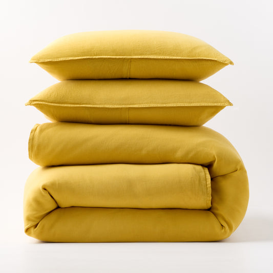 Stacked yellow European washed linen duvet cover and two matching pillow shams on a white background.