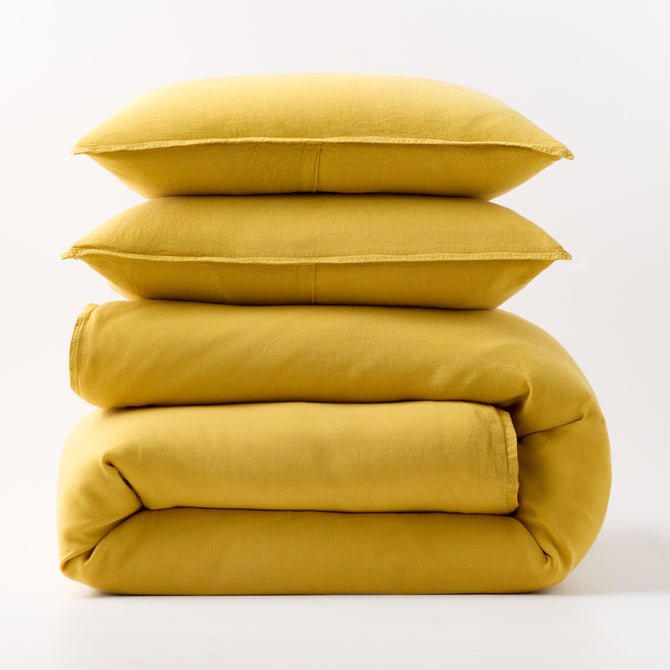 Stacked yellow European washed linen duvet cover and two matching pillow shams on a white background.
