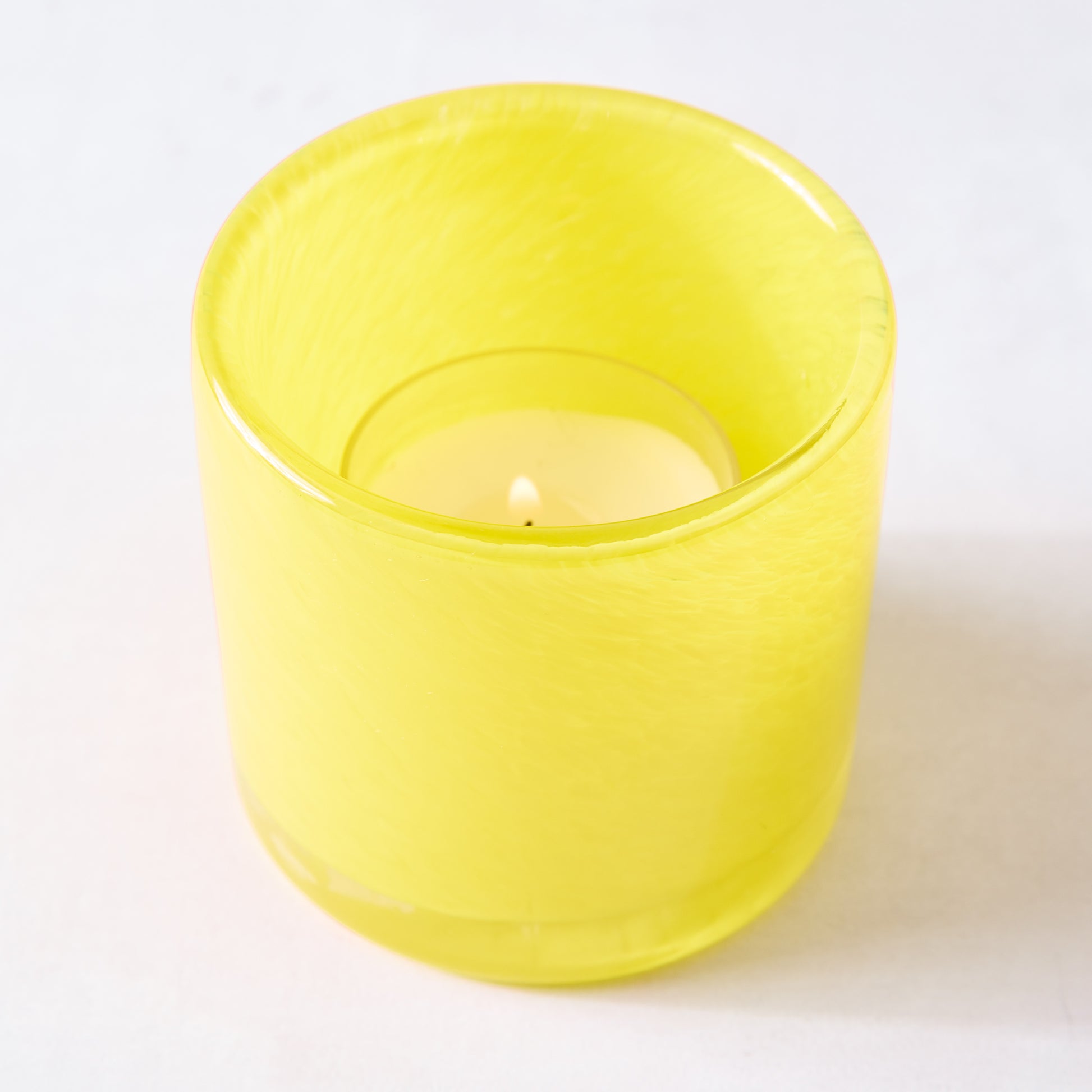 Bright yellow glass votive candle holder with a lit tealight inside, 2.75" tall.