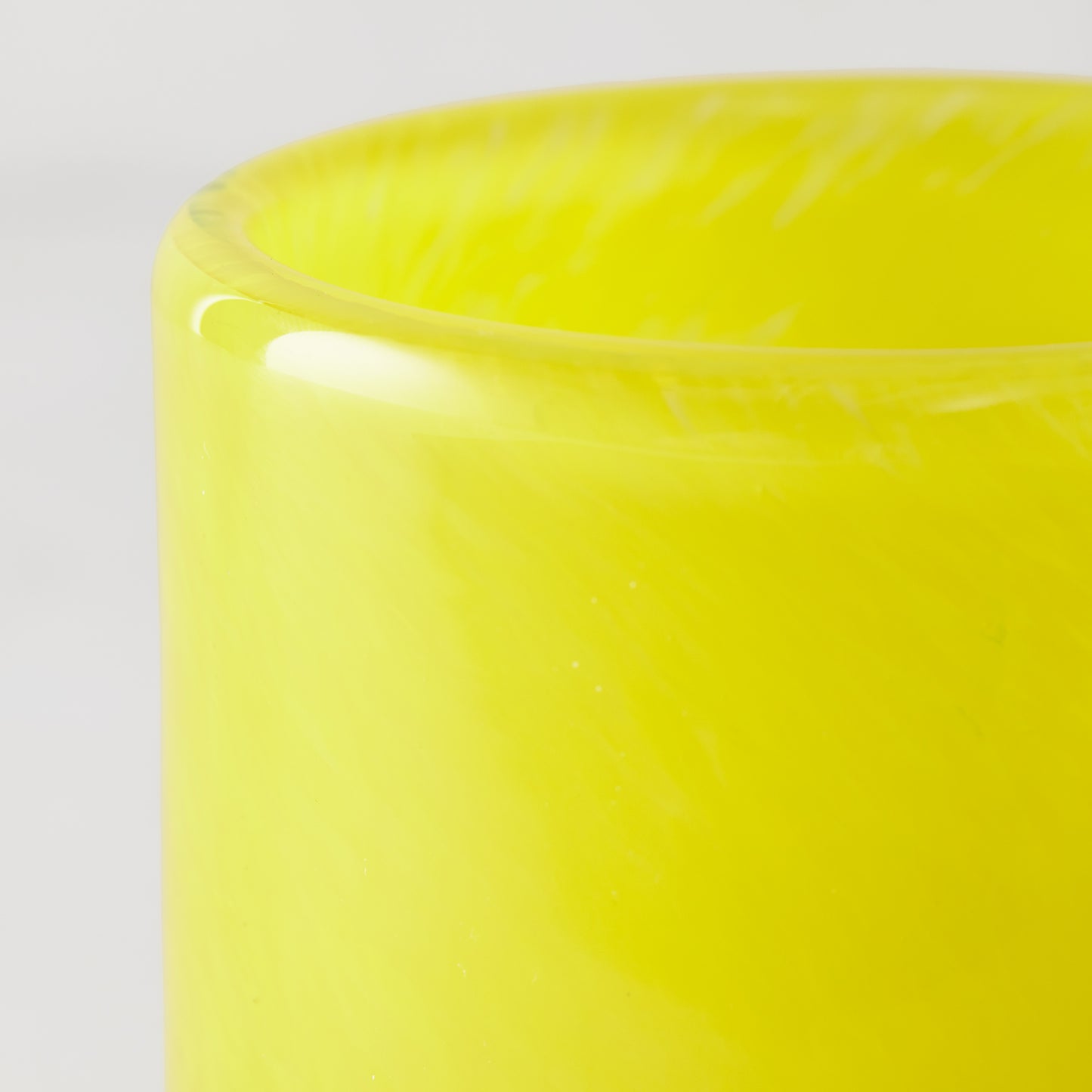 Bright yellow glass votive candle holder, close-up of smooth rim and vibrant hue.