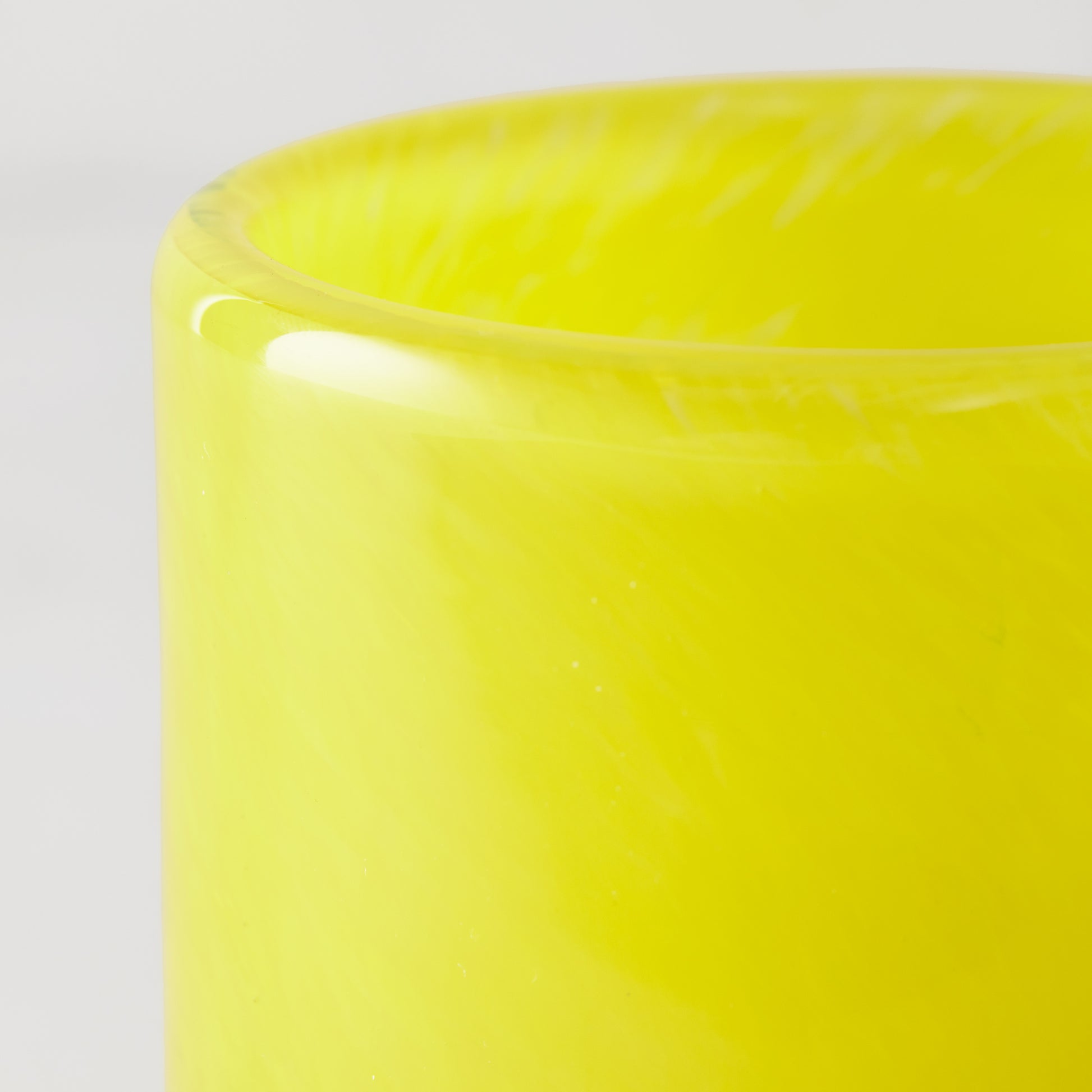 Bright yellow glass votive candle holder, close-up of smooth rim and vibrant hue.