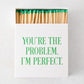 White oversized matchbox with "YOU'RE THE PROBLEM. I'M PERFECT." in green text, filled with long matches with green tips.
