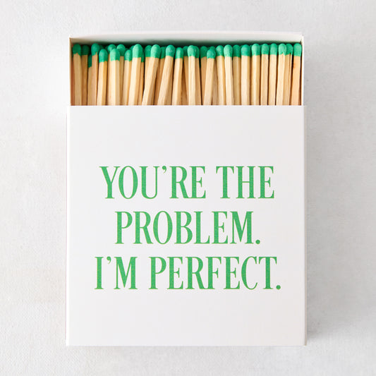 White oversized matchbox with "YOU'RE THE PROBLEM. I'M PERFECT." in green text, filled with long matches with green tips.