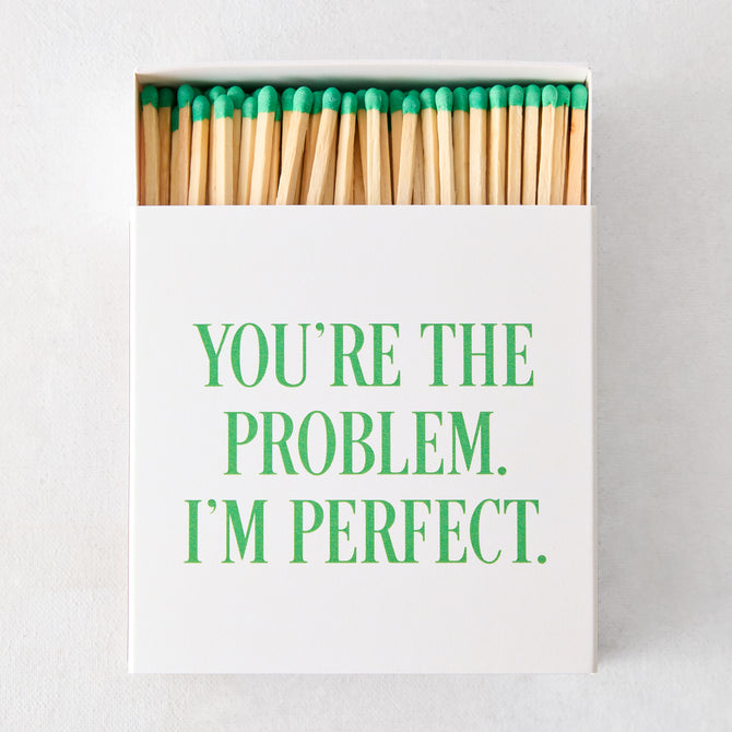 White oversized matchbox with "YOU'RE THE PROBLEM. I'M PERFECT." in green text, filled with long matches with green tips.