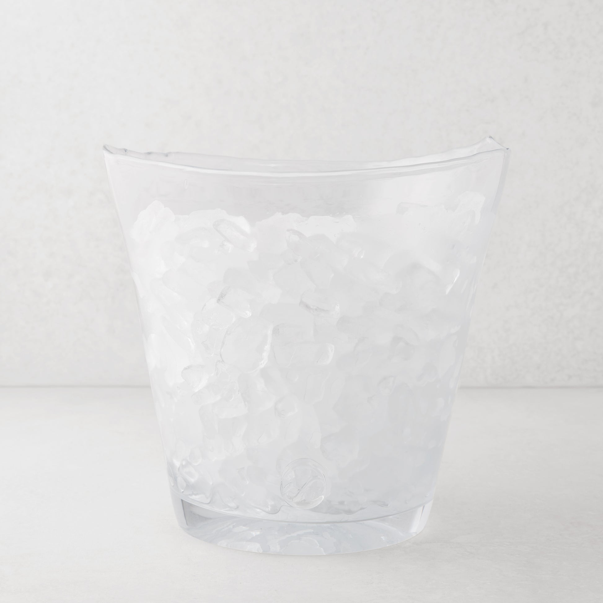 Clear mouth-blown glass Zion oversized ice bucket with scissor-cut rim, filled with ice.