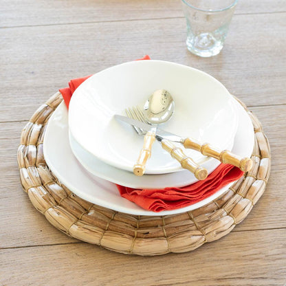 Bamboo 5-piece flatware set with 18/10 stainless steel, natural bamboo handles on white plates, red napkin, woven placemat.