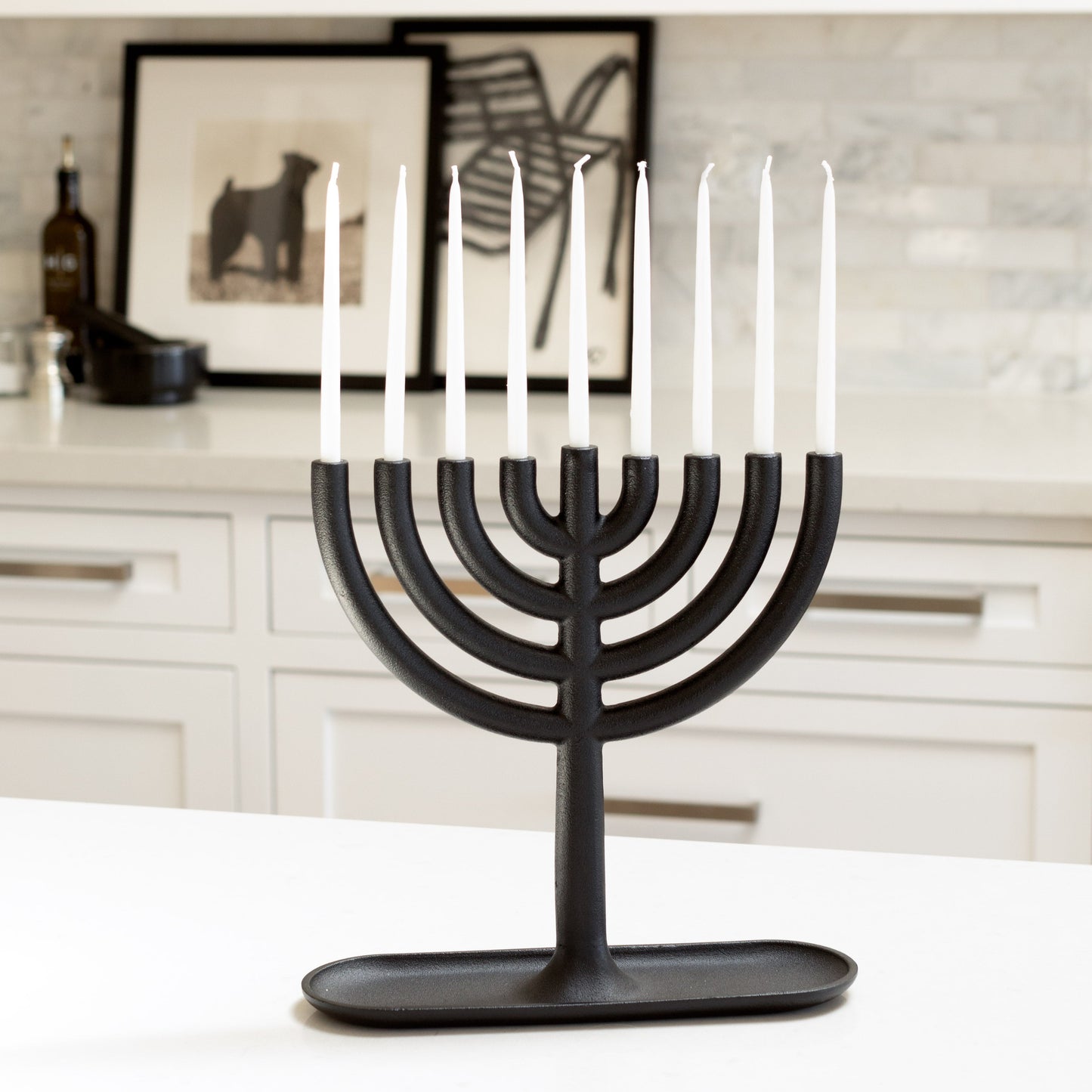 Black cast iron Hanukkah menorah by Josh Owen with white taper candles on a white counter.