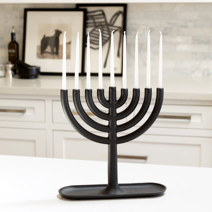 Black cast iron Hanukkah menorah by Josh Owen with white taper candles on a white counter.