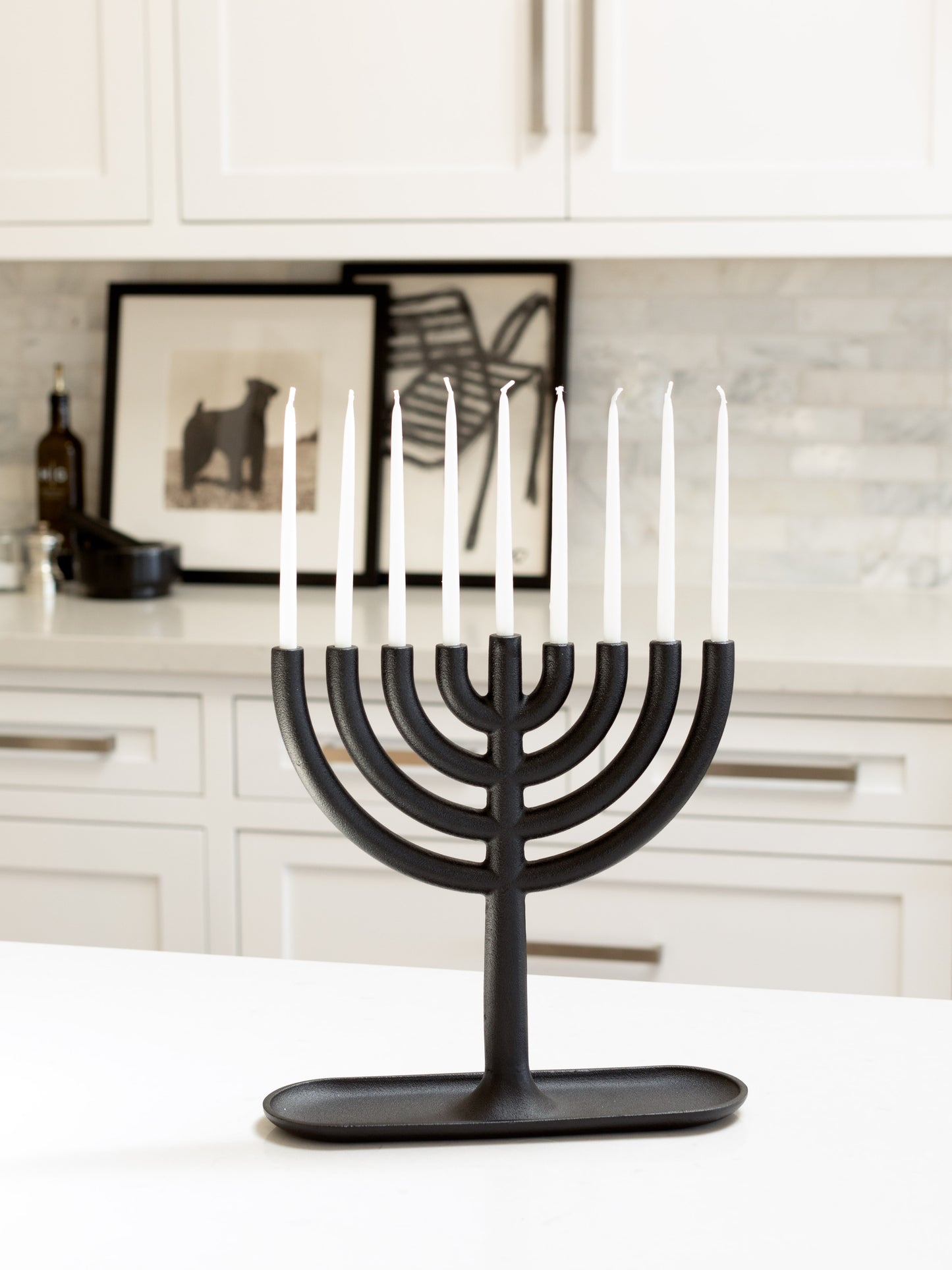 Black cast iron Hanukkah menorah by Josh Owen with white taper candles on a white counter.
