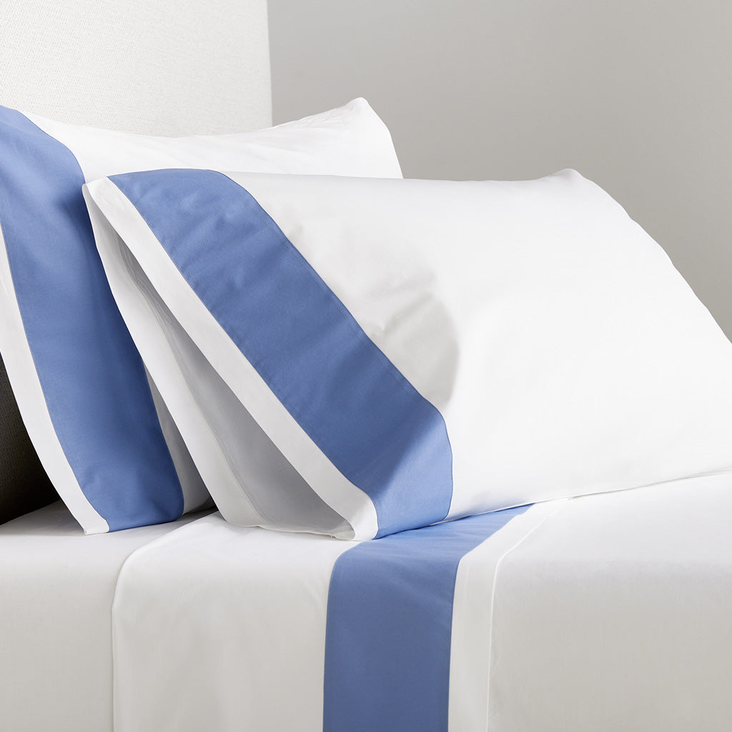 White percale pillowcases with a wide blue appliqued band, set of 2, on a bed.