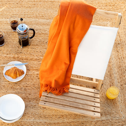 Bright orange cashmere throw blanket with fringe draped over a wooden chair.