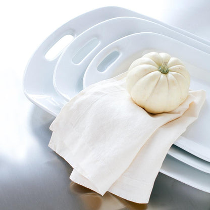 Three white ceramic serving platters with handles, stacked, with a small white pumpkin on a linen napkin.