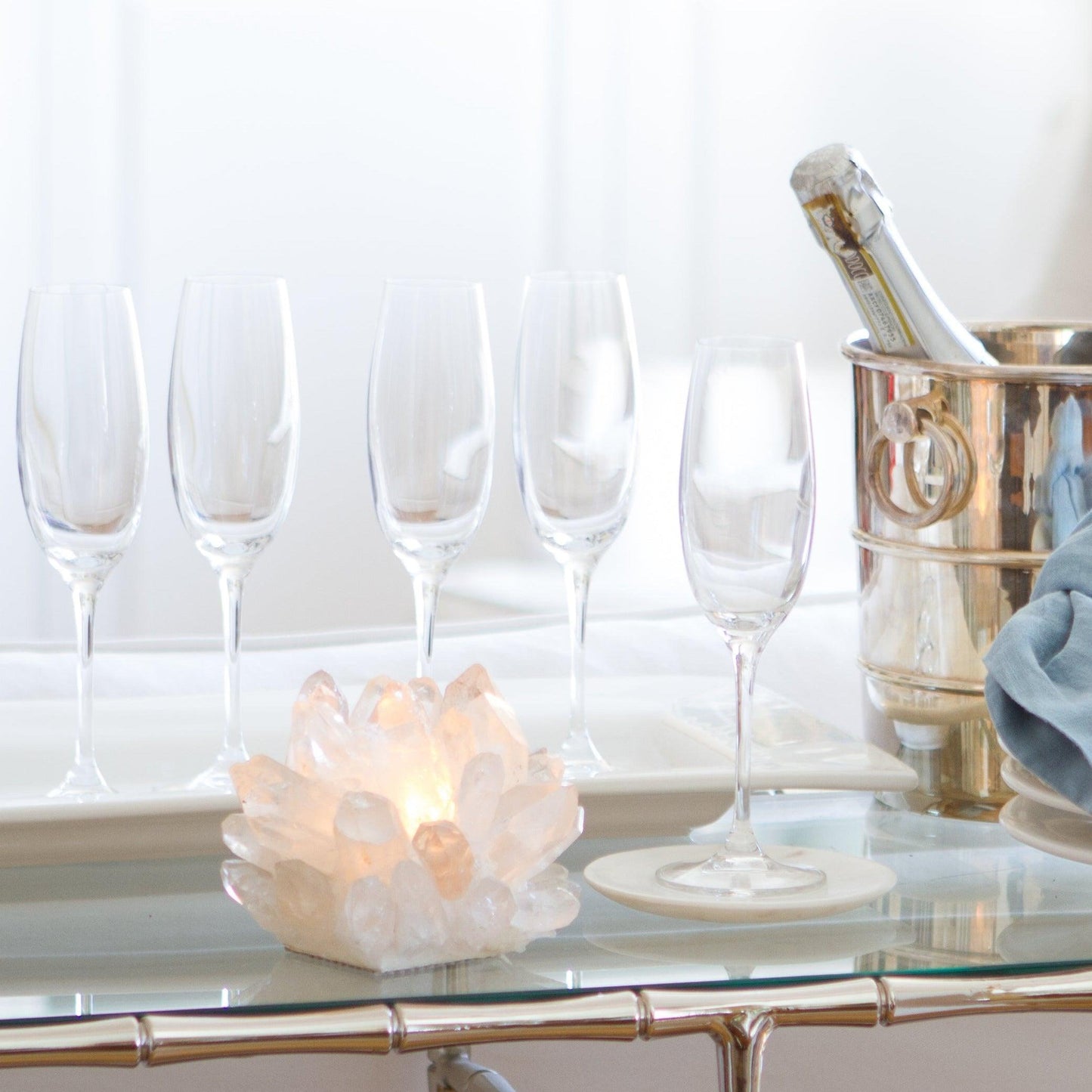 Clear Classic Quartz Votive Candle Holder with a lit candle, surrounded by champagne flutes and a wine cooler.
