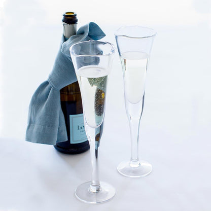Cloudy HG Signature hand-dyed linen napkin tied around a champagne bottle, with two flutes of bubbly.