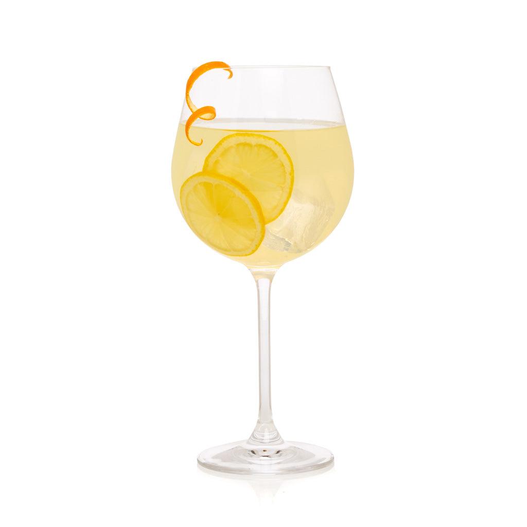Crystal stemmed wine glass with a light yellow drink, lemon slices, and an orange peel garnish.