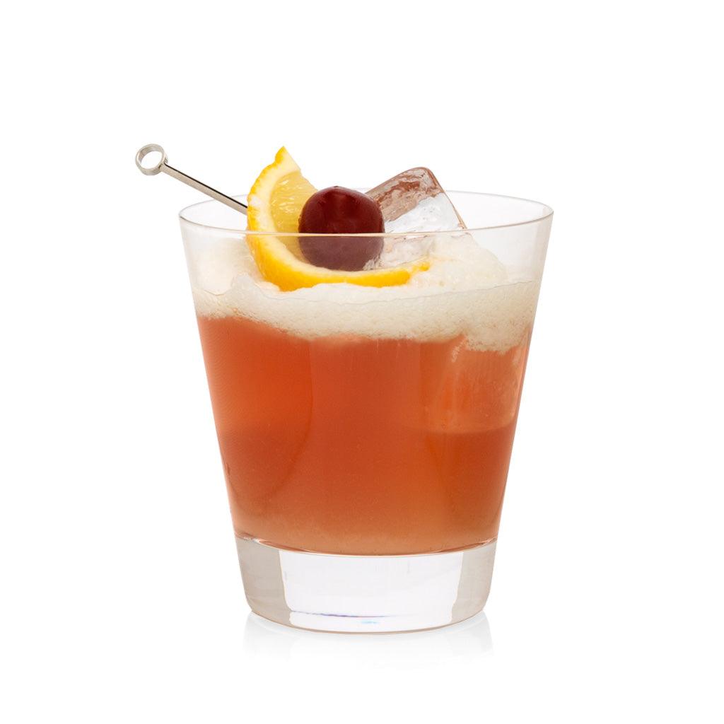 Crystal whiskey glass with orange-red drink, white foam, lemon slice, cherry, and ice cube.