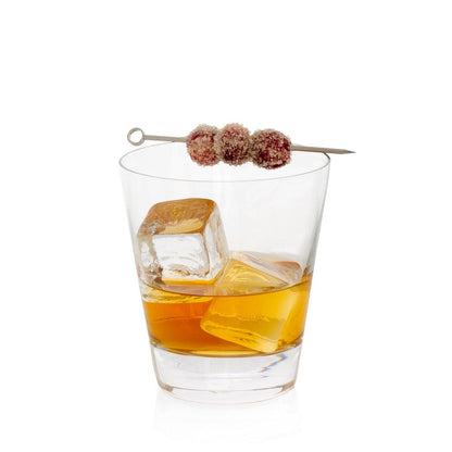 Crystal whiskey glass with amber liquid, ice cubes, and sugared cranberries on a metal skewer.