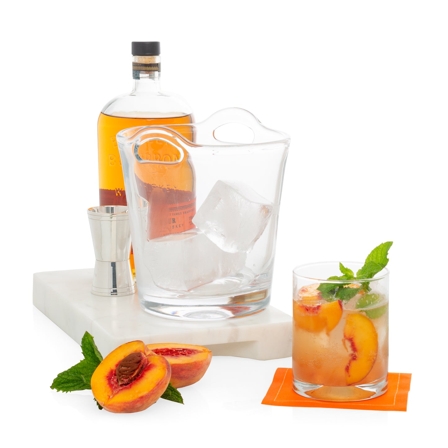 Clear Hudson Grace Double Old-Fashioned Glass with peach cocktail, whiskey bottle, ice bucket, and fresh peaches.
