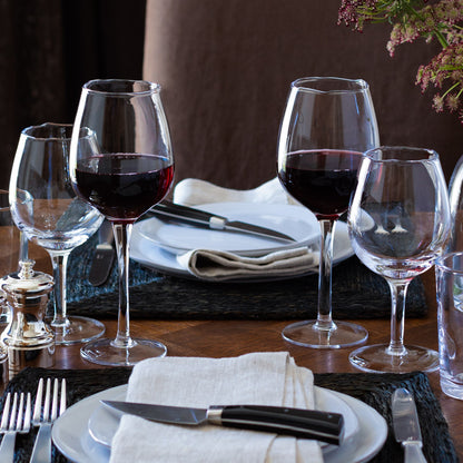 Two Elijah Large Scissor-Cut Wine Glasses, 14 oz, filled with red wine on a set dining table.