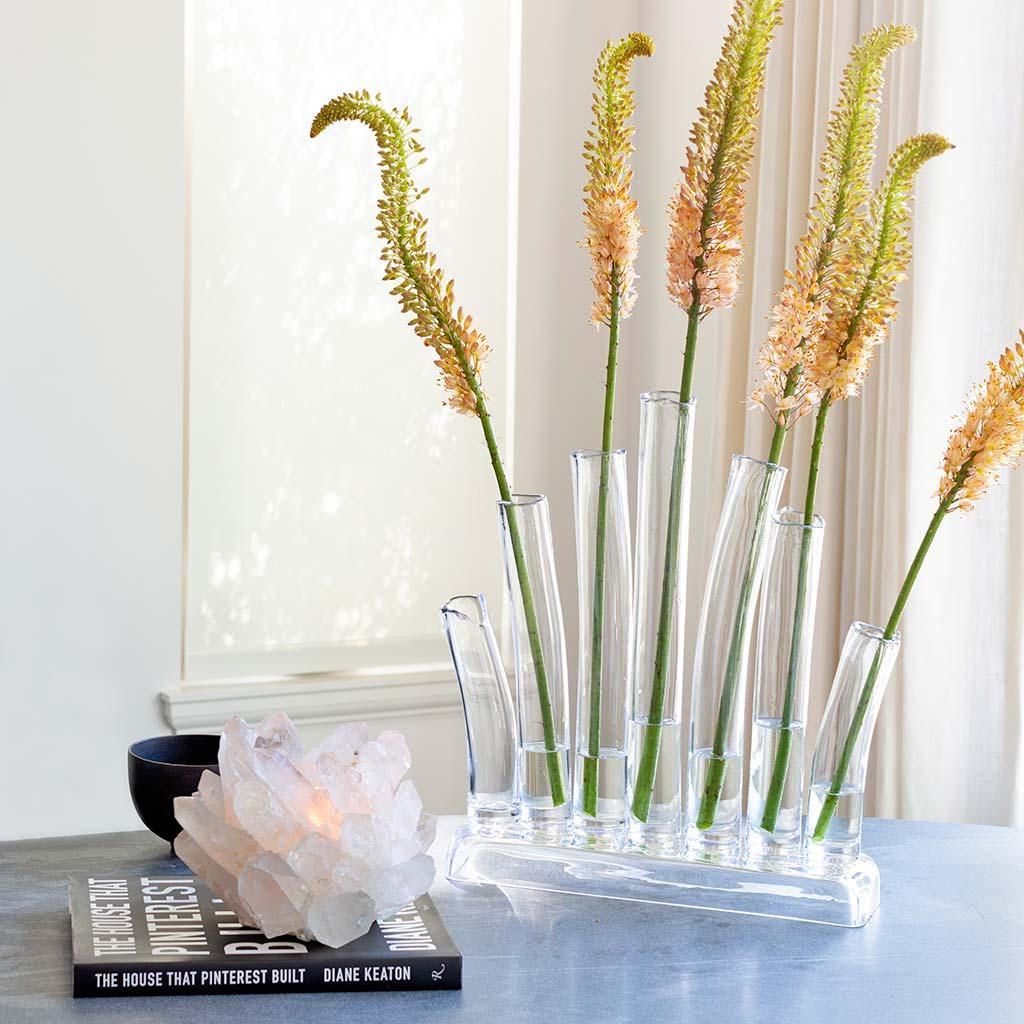 Large clear glass Elli vase with multiple scissor-cut tubes holding yellow-orange stems.
