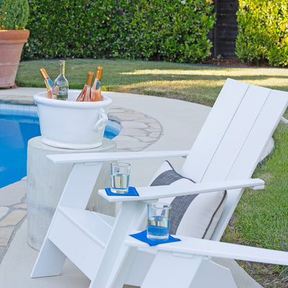 Two white Adirondack chairs by a pool, each with a glass of water on a blue coaster. A white ice bucket with wine bottles sits nearby.