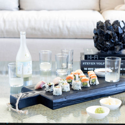 Clear, simple Everyday Wine Glasses on a glass table with sushi, sake, and a dark serving board.