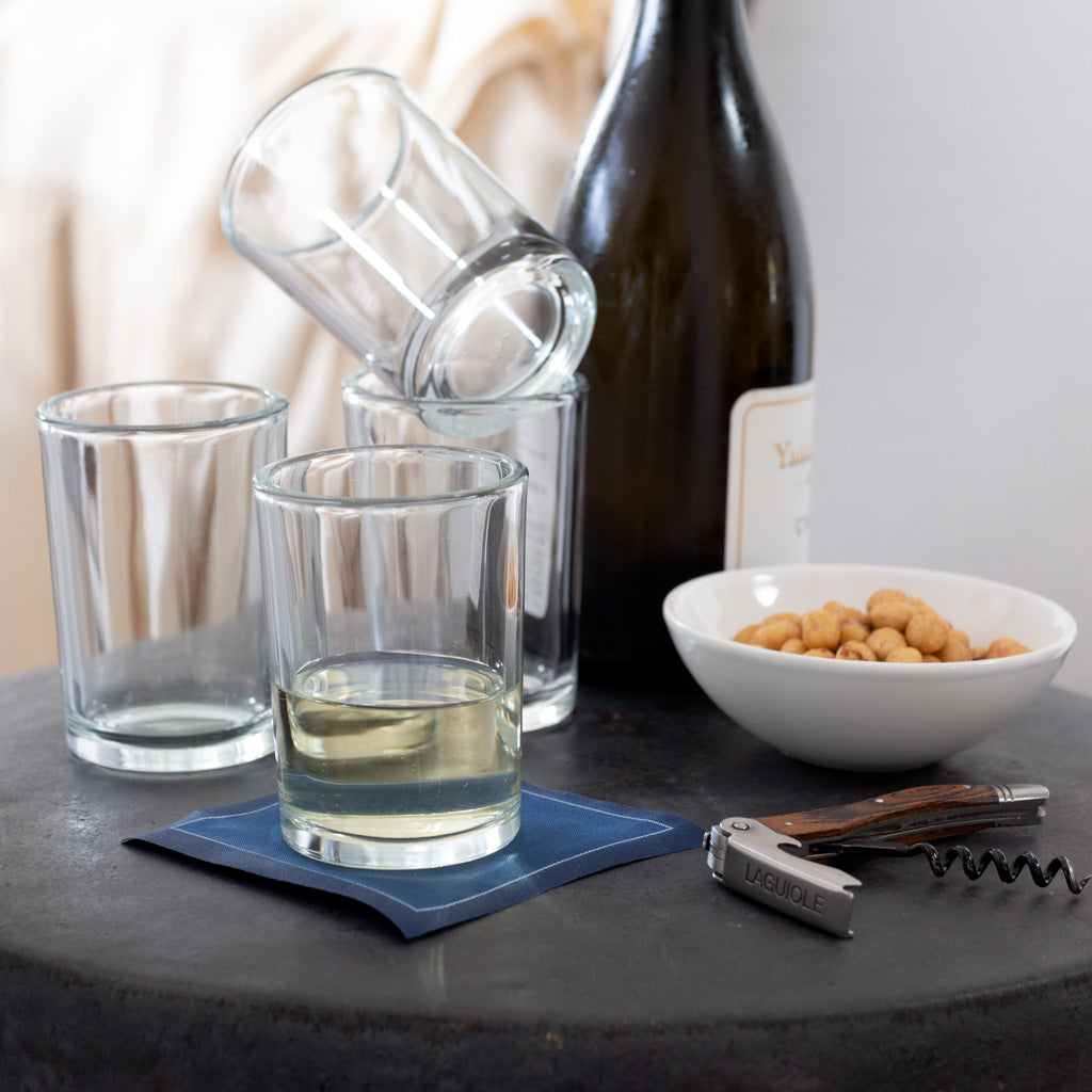 Clear, simple Everyday Wine Glasses, one with white wine, on a dark surface with a wine bottle and snacks.