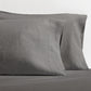 Set of two grey washed-linen pillowcases with double-needle stitching, resting on a grey sheet.