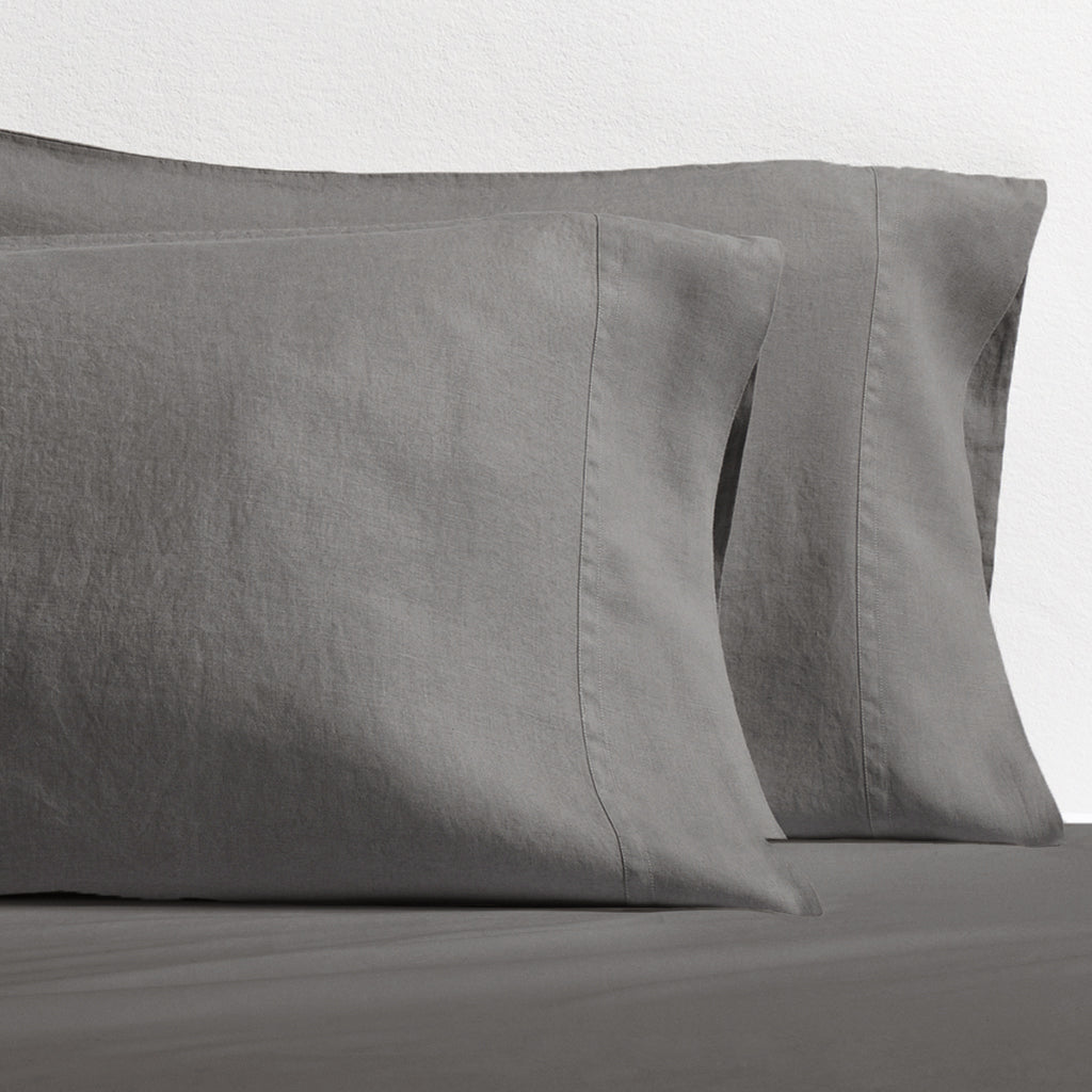 Set of two grey washed-linen pillowcases with double-needle stitching, resting on a grey sheet.