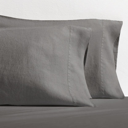 Set of two grey washed-linen pillowcases with double-needle stitching, resting on a grey sheet.