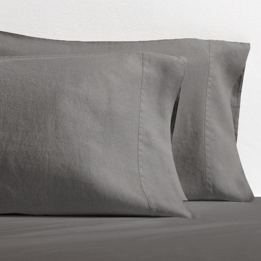 Set of two grey washed-linen pillowcases with double-needle stitching, resting on a grey sheet.