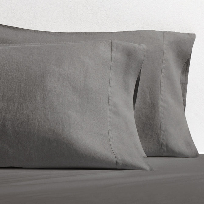 Set of two grey washed-linen pillowcases with double-needle stitching, resting on a grey sheet.
