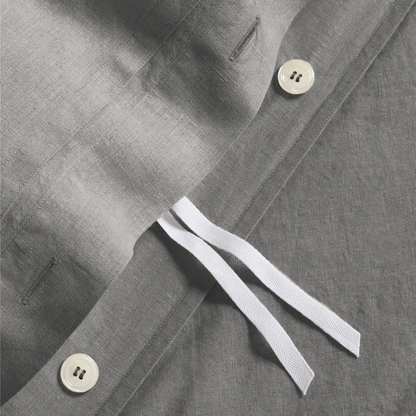 Close-up of a grey washed-linen duvet cover with hidden-button closure, white ties, and two cream buttons.