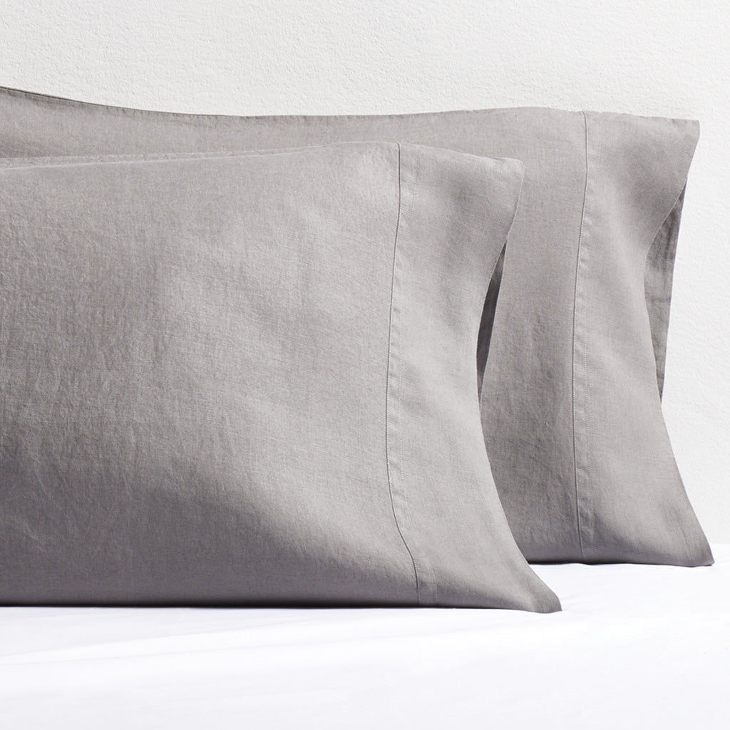 Two grey washed-linen pillowcases with double-needle stitch detailing, resting on a white sheet.