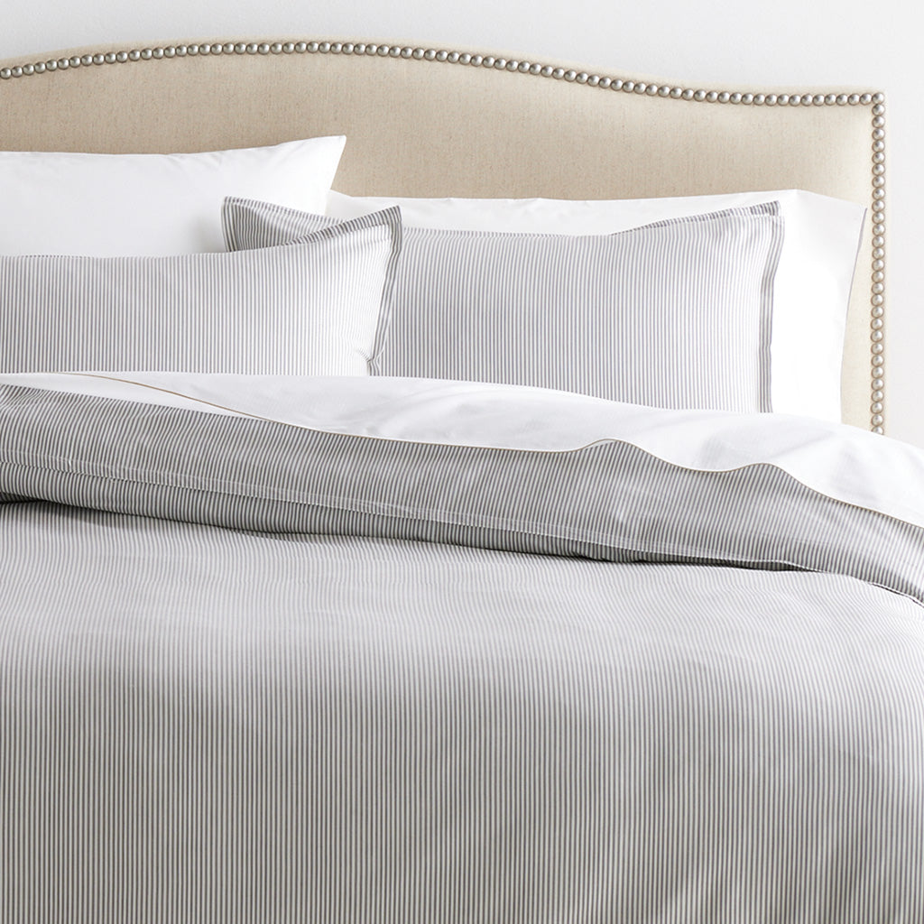 Set of 2 grey stripe cotton-chambray pillow shams with 2” flange and matching duvet cover on a bed.