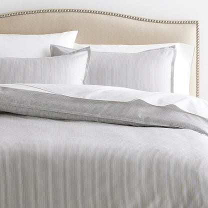 Set of 2 grey stripe cotton-chambray pillow shams with 2” flange and matching duvet cover on a bed.