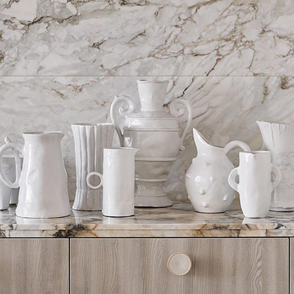 Handmade creamy white ceramic bumpy pitcher 5163 by Montes Doggett, surrounded by other white ceramic vessels on a marble counter.