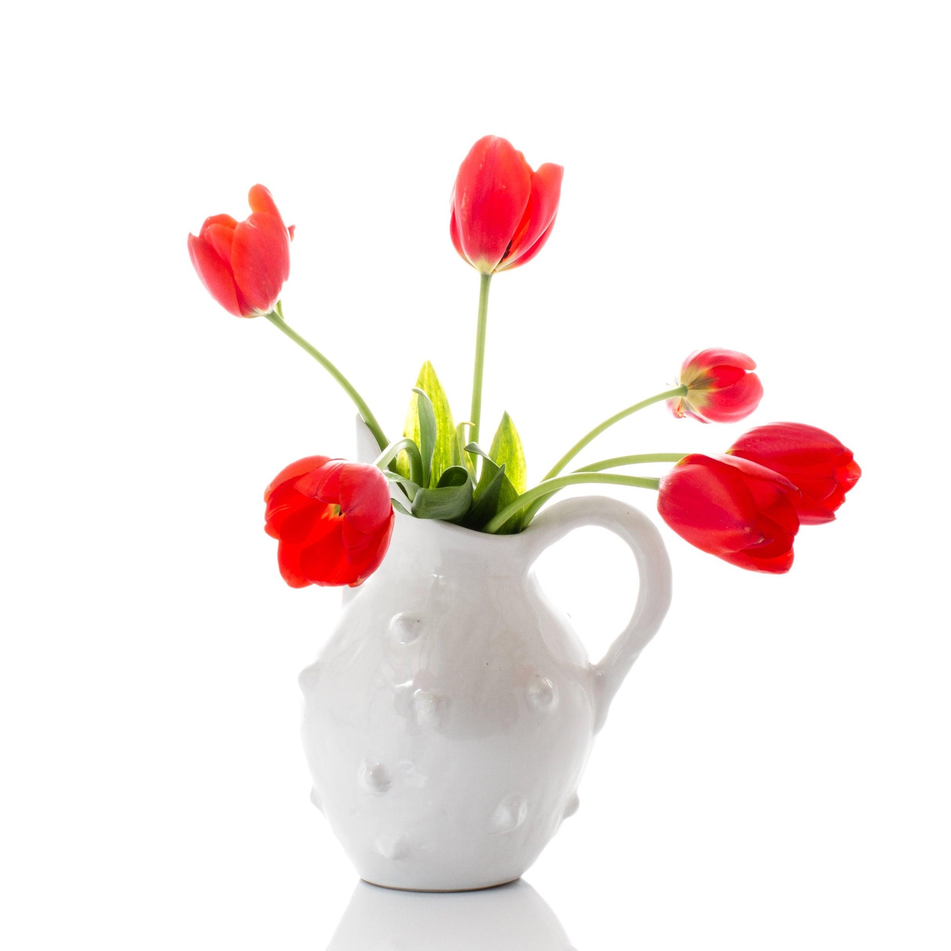 Handmade creamy white ceramic bumpy pitcher by Montes Doggett with red tulips.