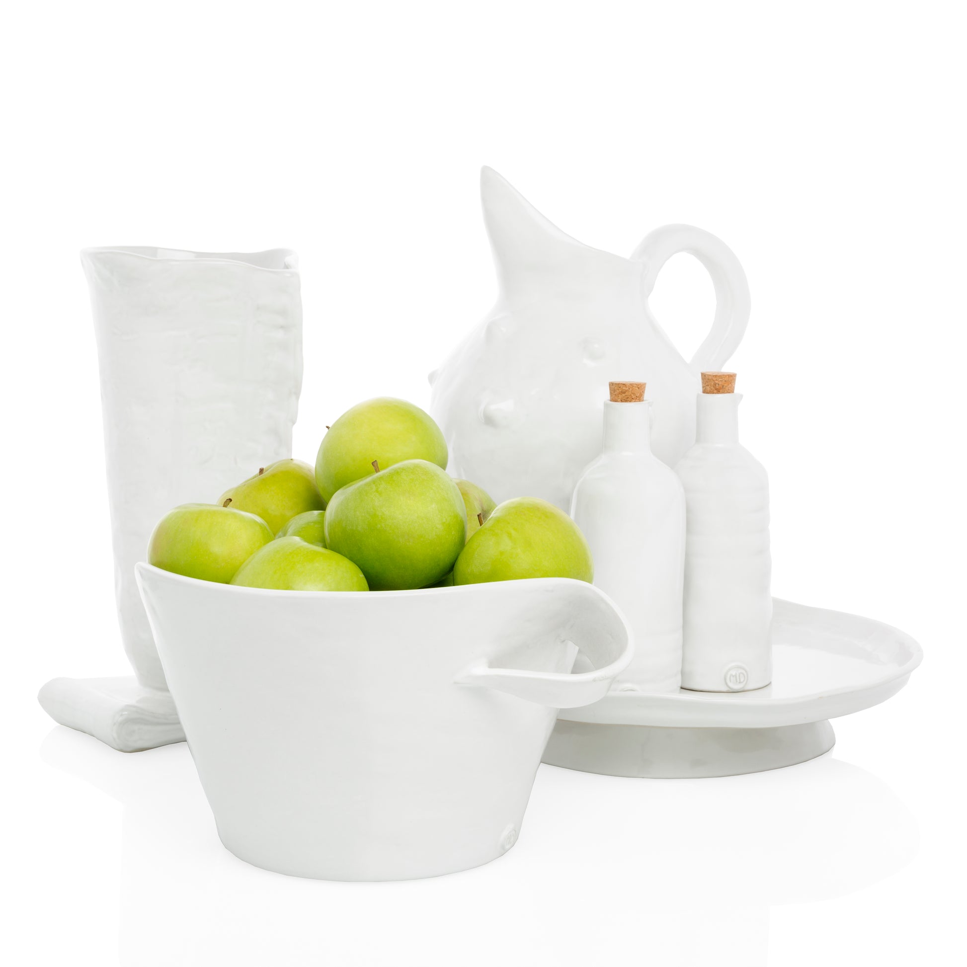 Handmade creamy white ceramic serve bowl by Montes Doggett, filled with green apples, alongside matching pottery.