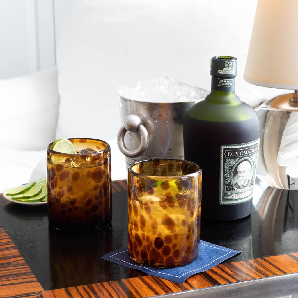 Handmade 12 oz. amber and brown tortoise double old-fashioned glasses with cocktails, ice bucket, and rum bottle.